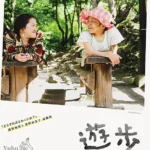安積遊步坐在輪椅上與年輕介助者交流，神情堅定平靜